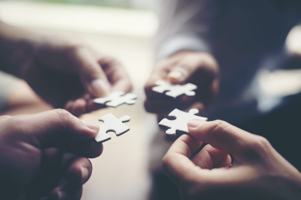 Vier Hände, die je ein Puzzleteil gegeneinanderhalten, Partnerschaft.