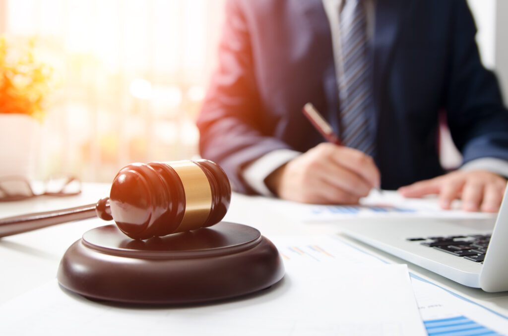 Hölzerner Richterhammer auf einem Tisch, im Hintergrund eine Person mit Laptop, die auf einem Blatt schreibt als Symbol für die Laux Lawyers Case Study von baseVISION